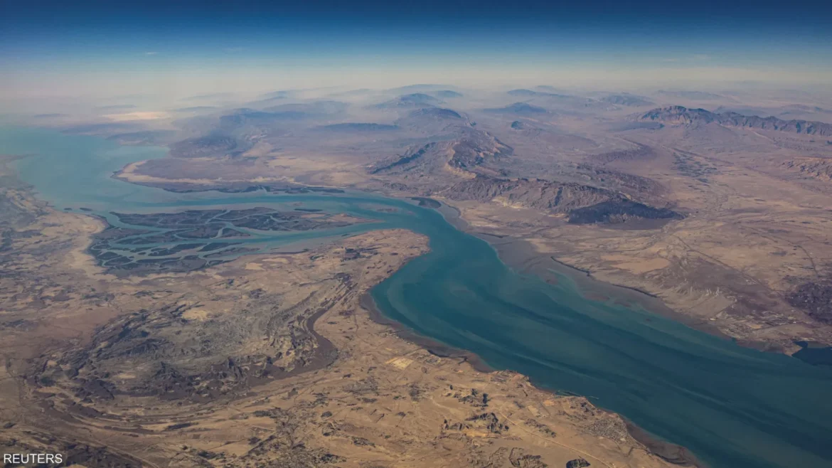 Aerial view of a winding turquoise river delta cutting through arid desert with distant mountains under a pale horizon.