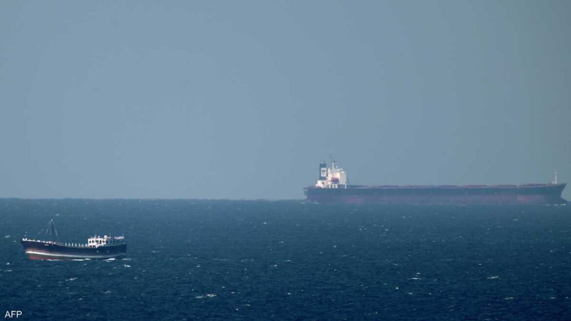 Small boat in the foreground with a large cargo ship visible on the horizon at sea.