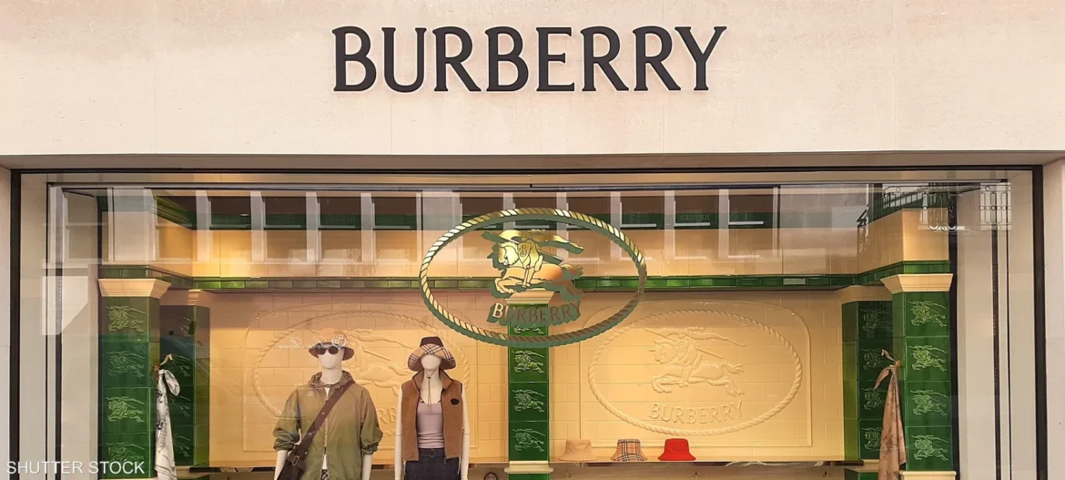Burberry storefront window display with the brand name above, mannequins wearing coats and hats amid a green-and-cream decor.