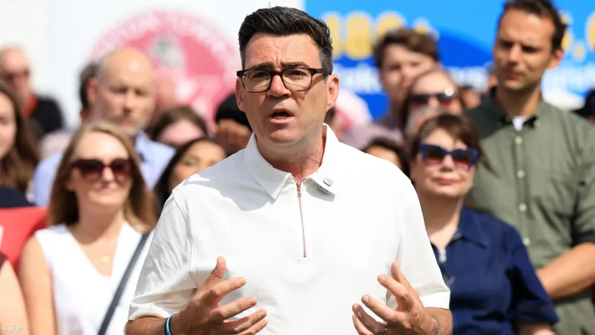 Man in a white polo shirt speaks to a crowd at an outdoor event, hands gesturing as onlookers stand behind him.