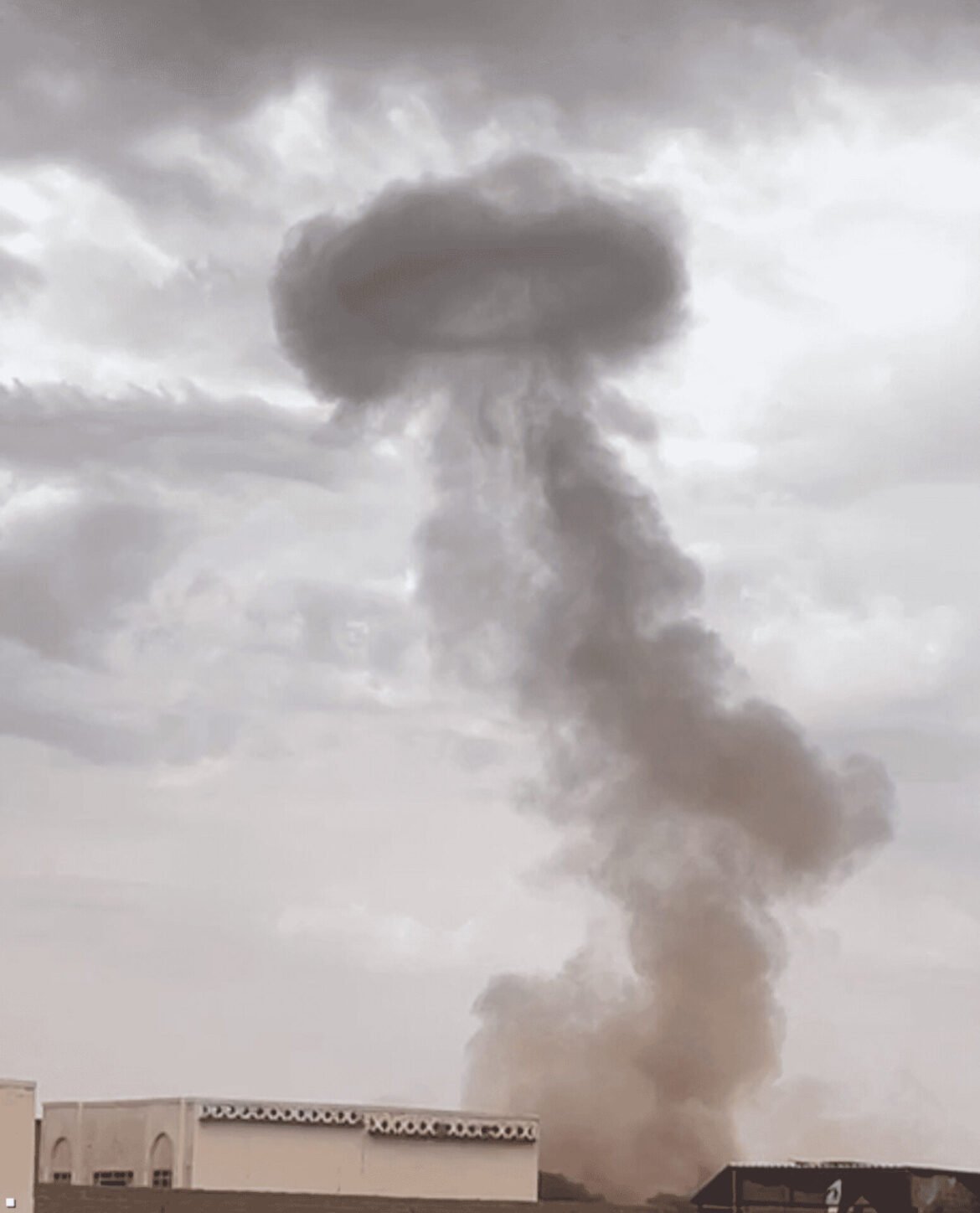 Smoke billows from a building, dark plume rising into the sky after a fire, with rooftops visible in the foreground.