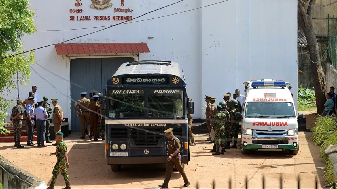 Prison transport scene outside a Sri Lankan facility: a dark blue bus labeled Sri Lanka Prison, security officers and soldiers gathered nearby, with an ambulance to the right.