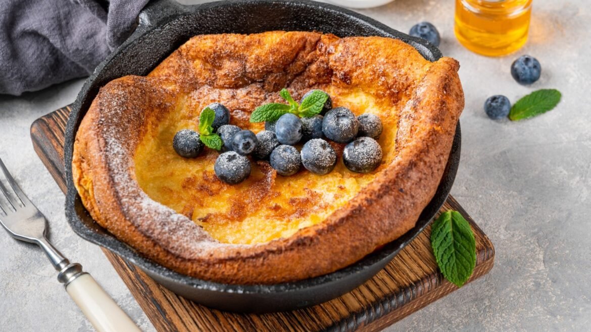 Cast-iron skillet with a golden Dutch baby pancake topped with blueberries and mint.