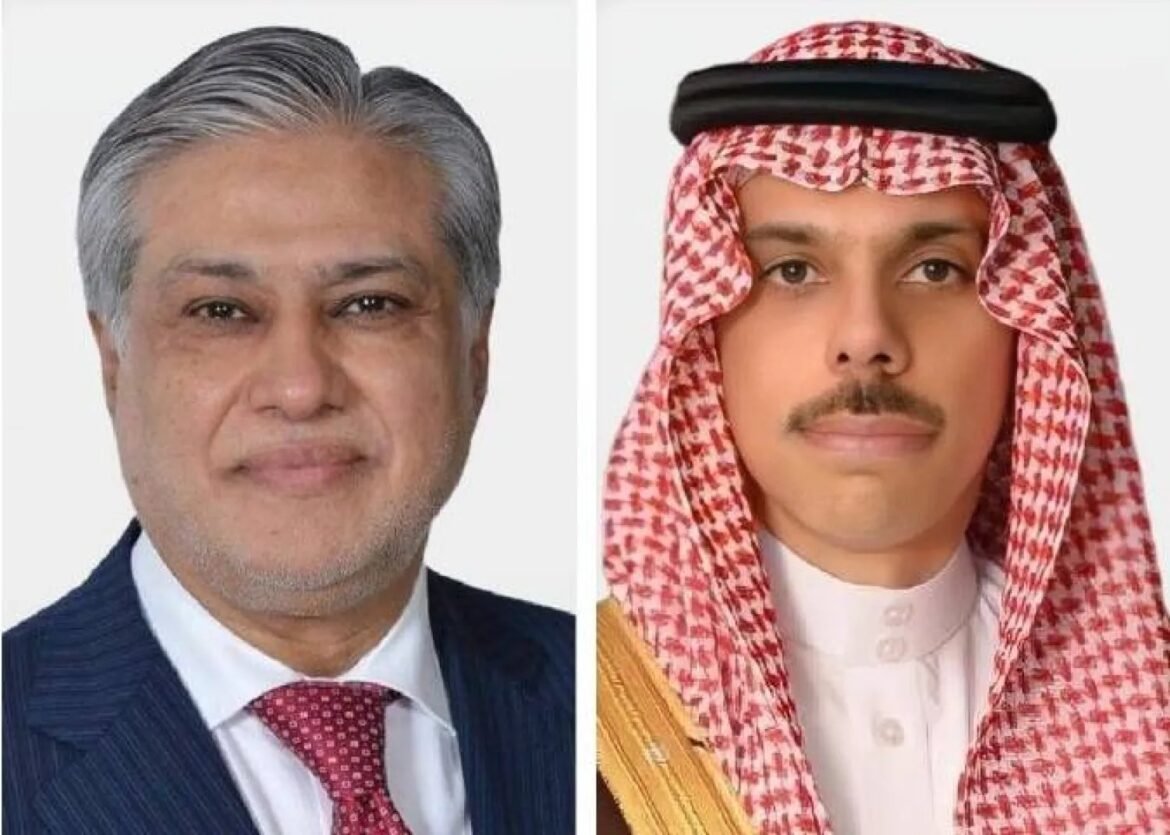 Two men side by side: left is a middle-aged man in a navy suit and red tie; right is a young man in a red-and-white keffiyeh with a black agal and white thobe.