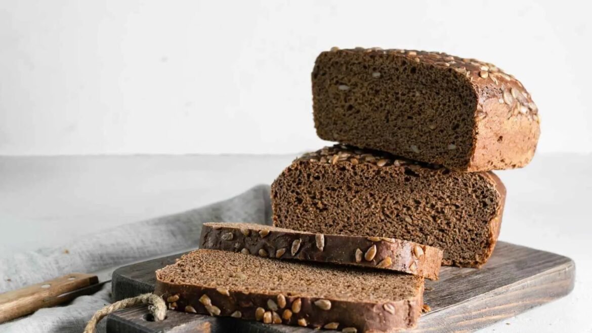 Dark seed-topped loaf on a wooden cutting board, with sliced pieces in front.