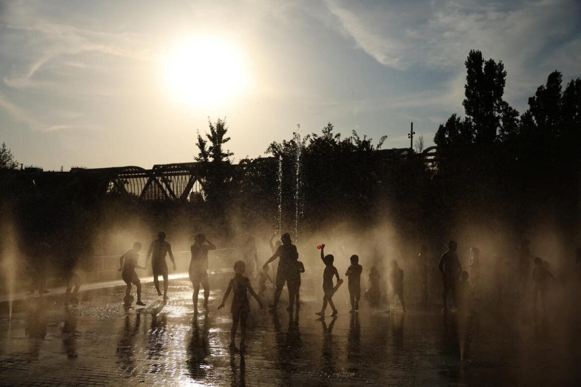 Children play in a misty fountain at sunset, silhouetted against a bright sky.