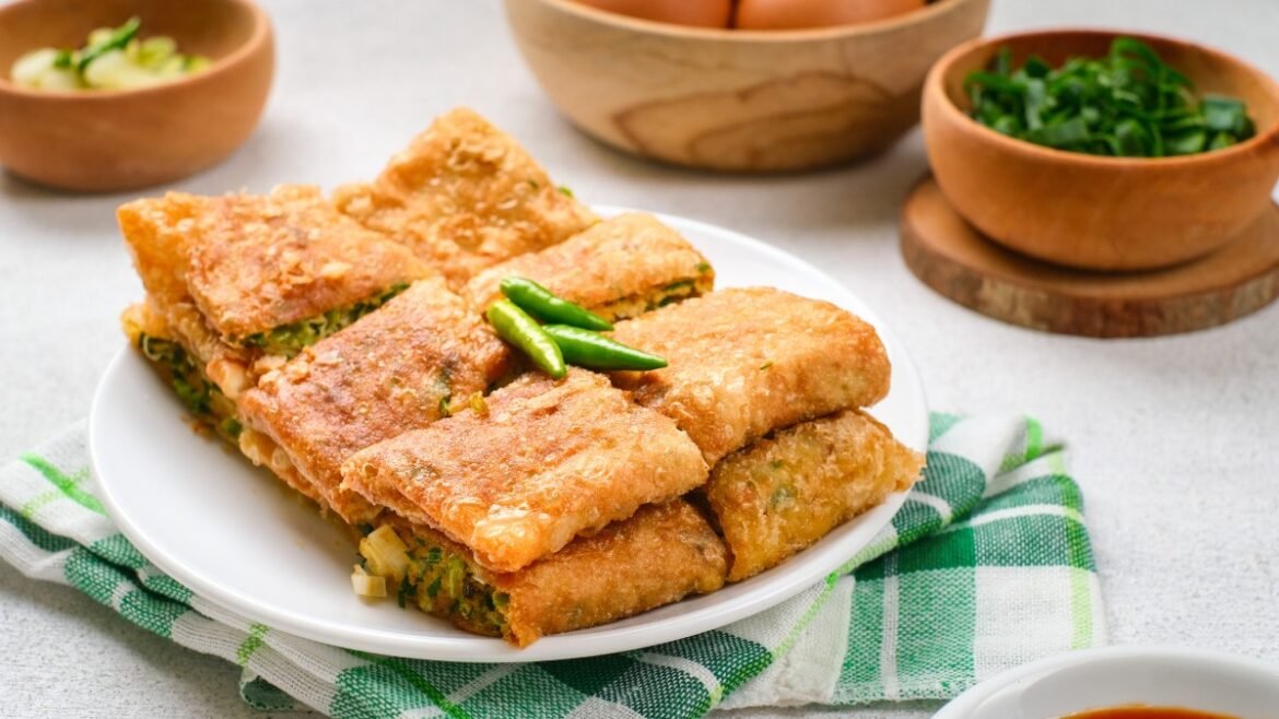 Plate of golden-brown fried flatbread rectangles stuffed with greens, topped with two green chilies.