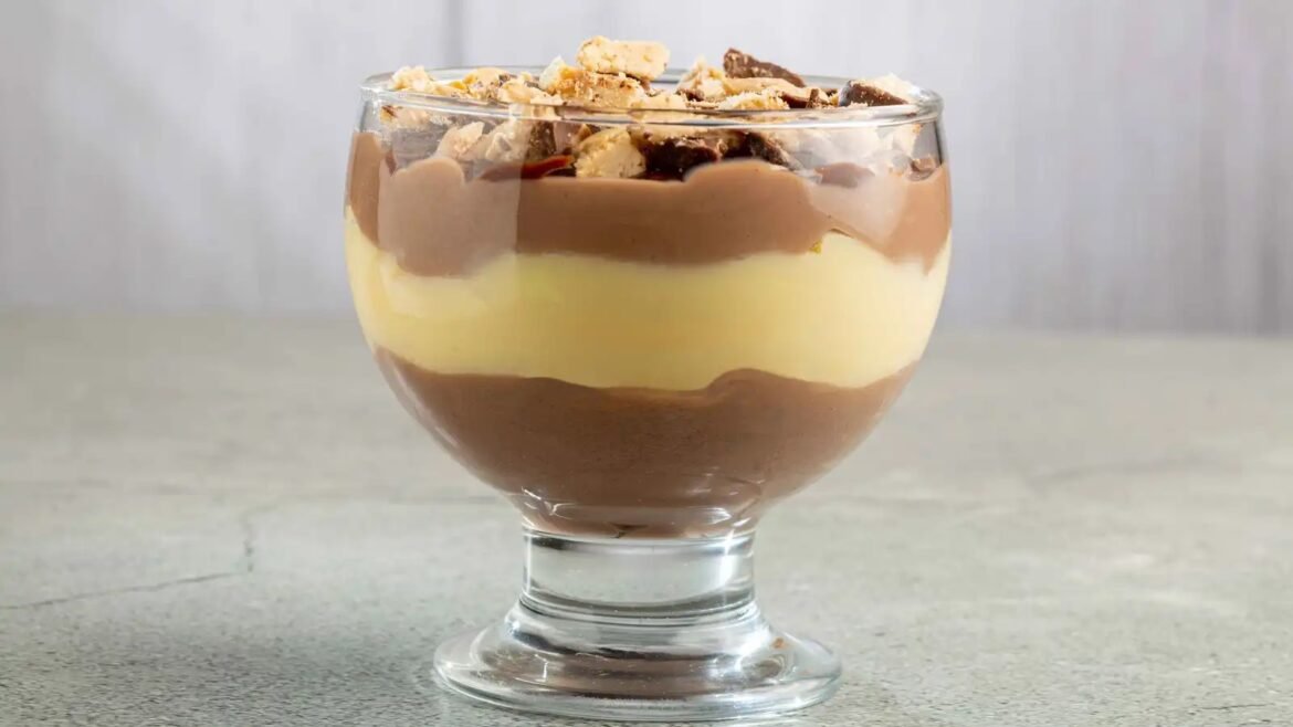 Layered chocolate and vanilla dessert parfait in a clear glass with crunchy topping on top.