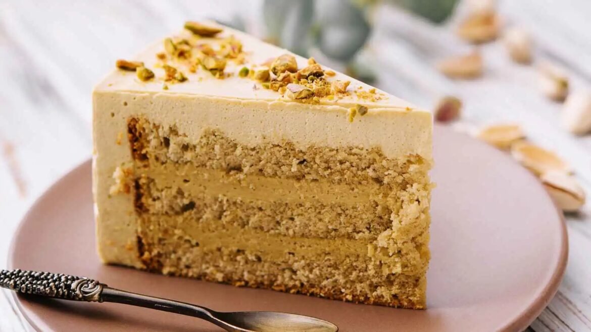 Slice of layered cake with a crumbly nut topping on a pink plate, a silver spoon in the foreground.