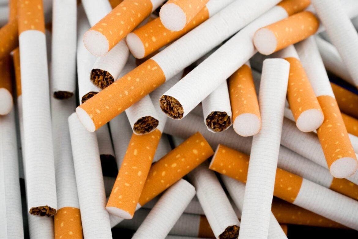 Close-up of a heap of cigarettes with white bodies and orange filters showing at the ends.