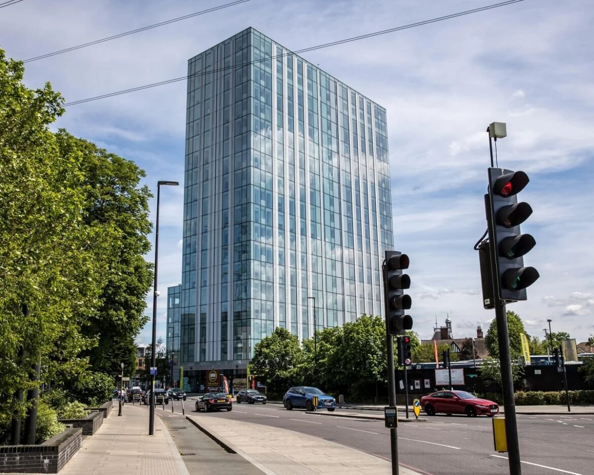 Tall glass-office building with blue-tinted windows along a busy urban street, traffic lights and cars in the foreground.