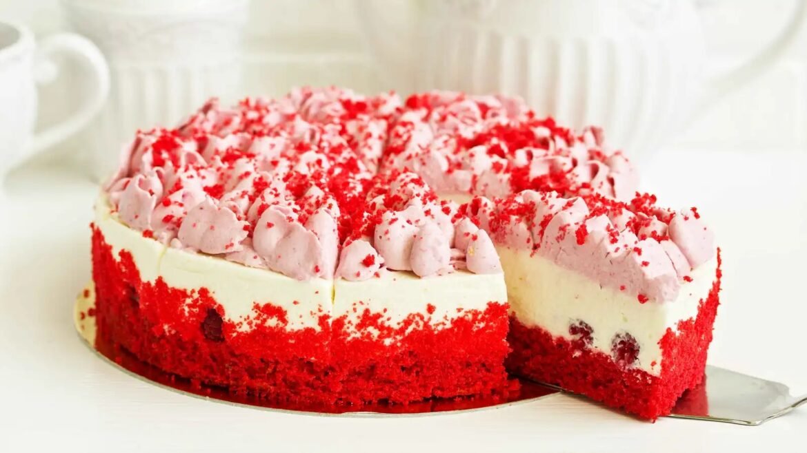 Red velvet cake with white frosting and pink whipped-cream rosettes, red sprinkles on top and along the sides, a slice removed to show layers
