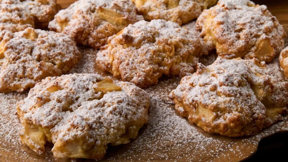Pile of crumbly apple fritters dusted with powdered sugar on a wooden board (dessert).