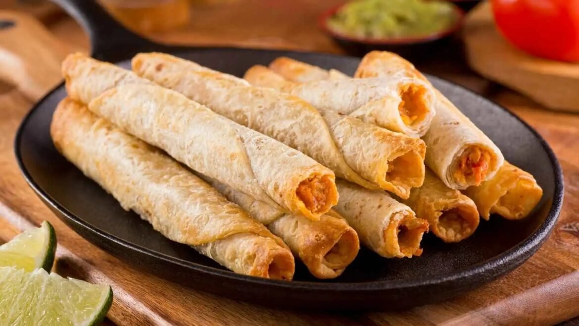 Crispy rolled taquitos with orange filling arranged on a black plate, lime wedges in the foreground.
