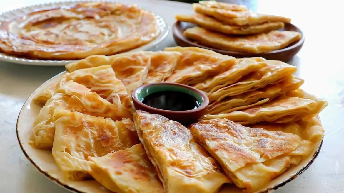 Golden flaky phyllo pastries arranged on plates with a small bowl of dark dipping sauce in the center.
