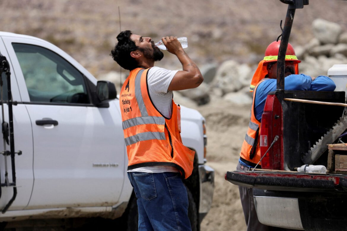 Construction worker in a bright safety vest drinks water beside a white pickup at an outdoor construction site.
