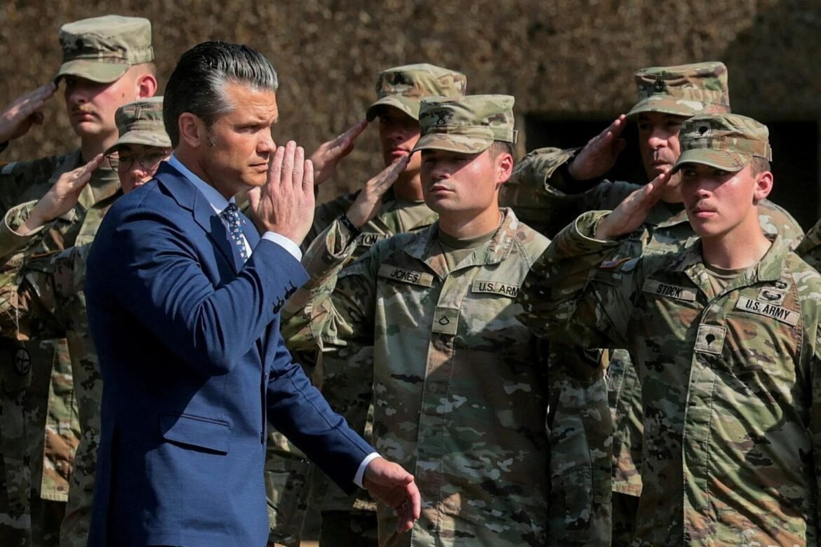 Civilian man in a blue suit salutes a line of camouflaged U.S. Army soldiers.