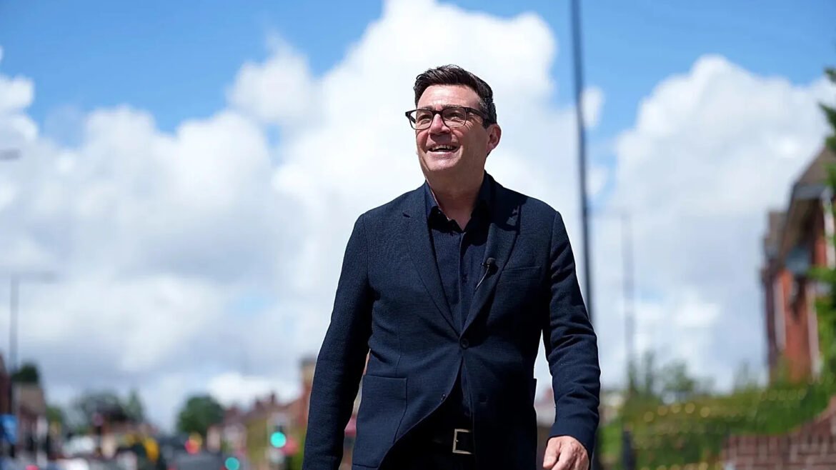 Man in a dark blazer walking outdoors on a sunny day, smiling against a bright, cloudy sky and urban street backdrop.