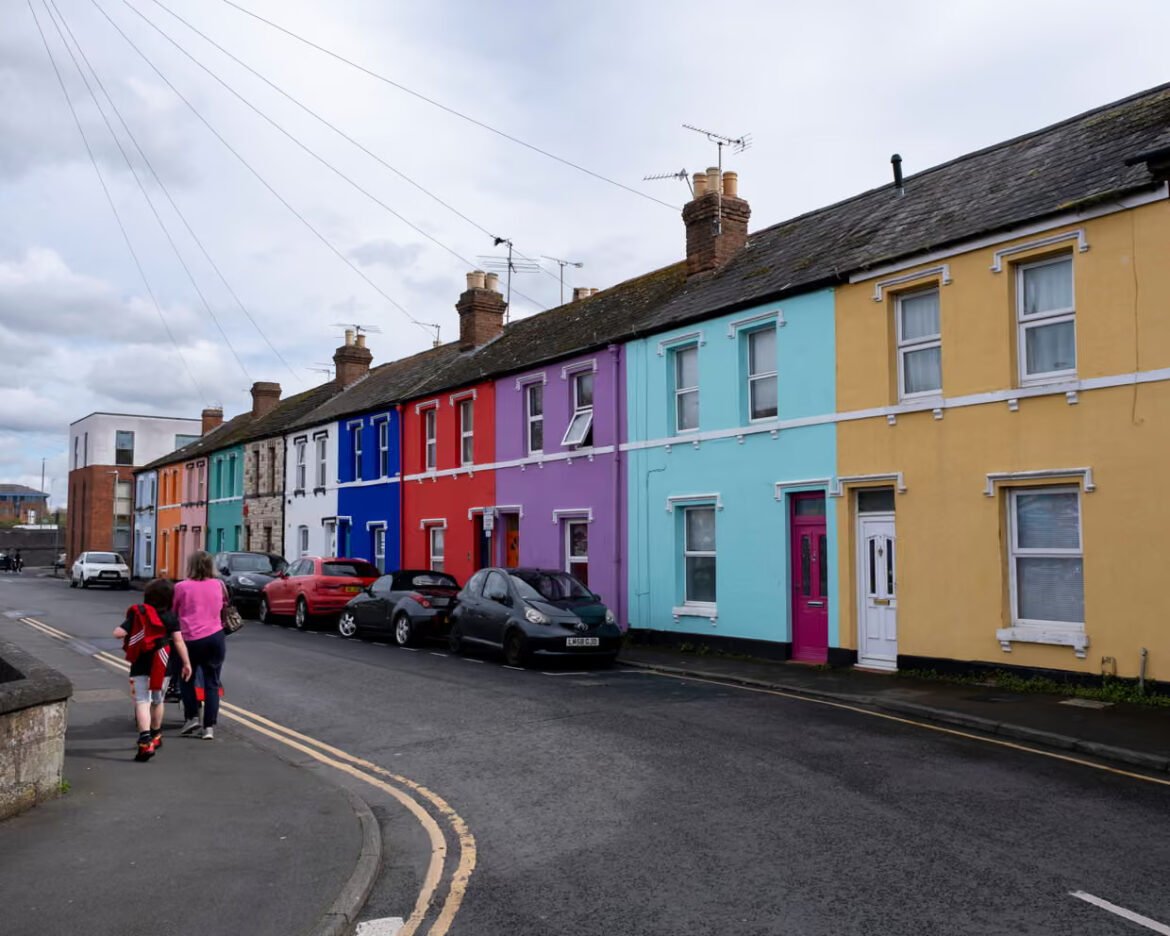 Row of brightly colored terraced houses along a street with parked cars and two children walking on the sidewalk in the foreground.