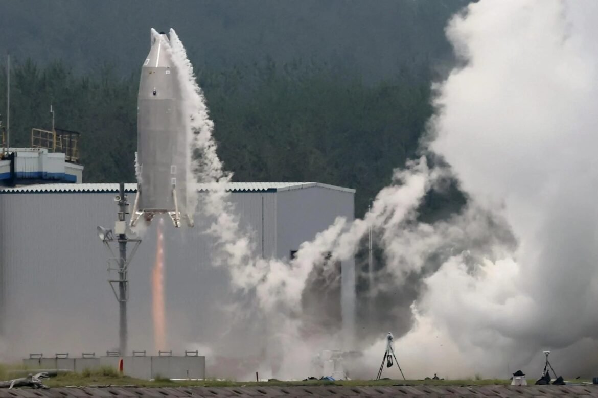 Rocket launching from pad with bright flame, surrounded by dense white exhaust and mist at a testing facility.