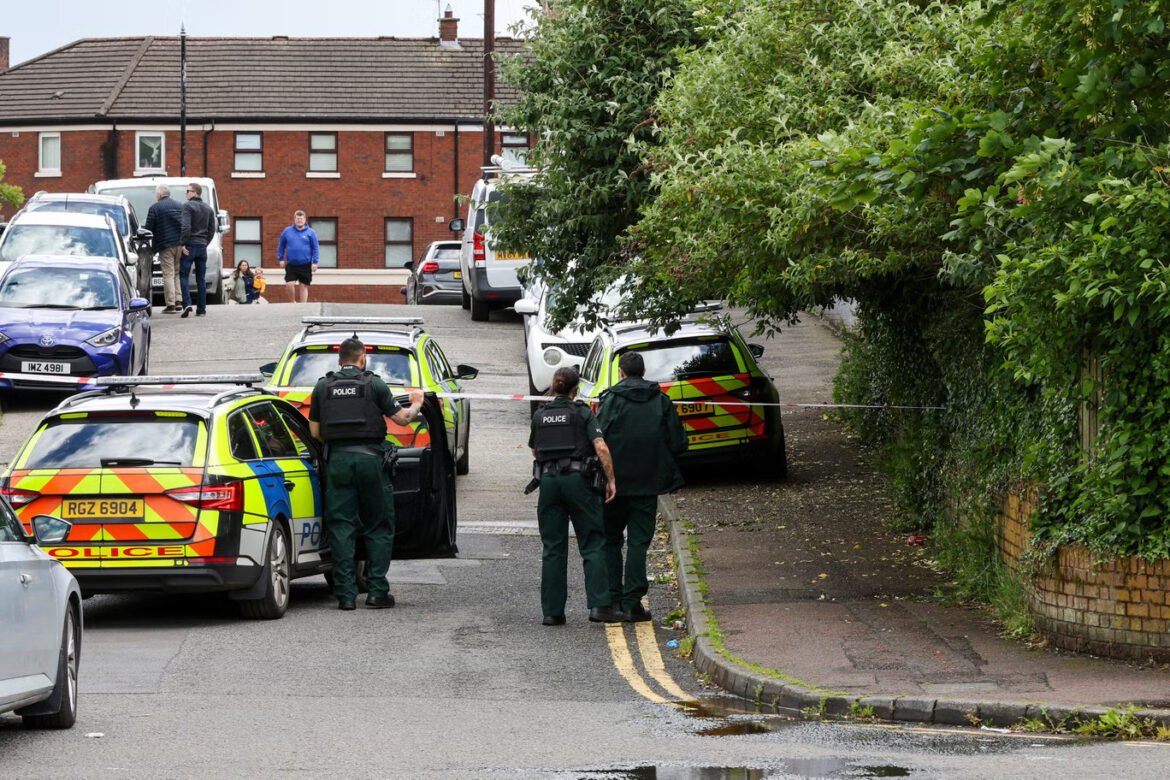 Police cars block a residential street with officers near a taped-off area.