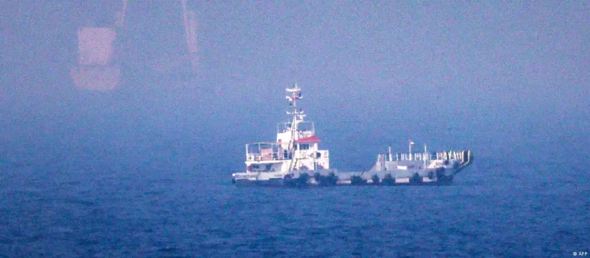 Small tugboat on a calm blue sea with a hazy horizon and red accents on the superstructure.