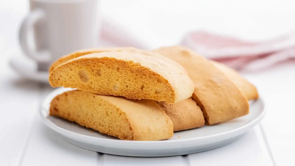 Stack of golden-brown cookies on a white plate with a blurred mug in the background, on a bright tabletop.
