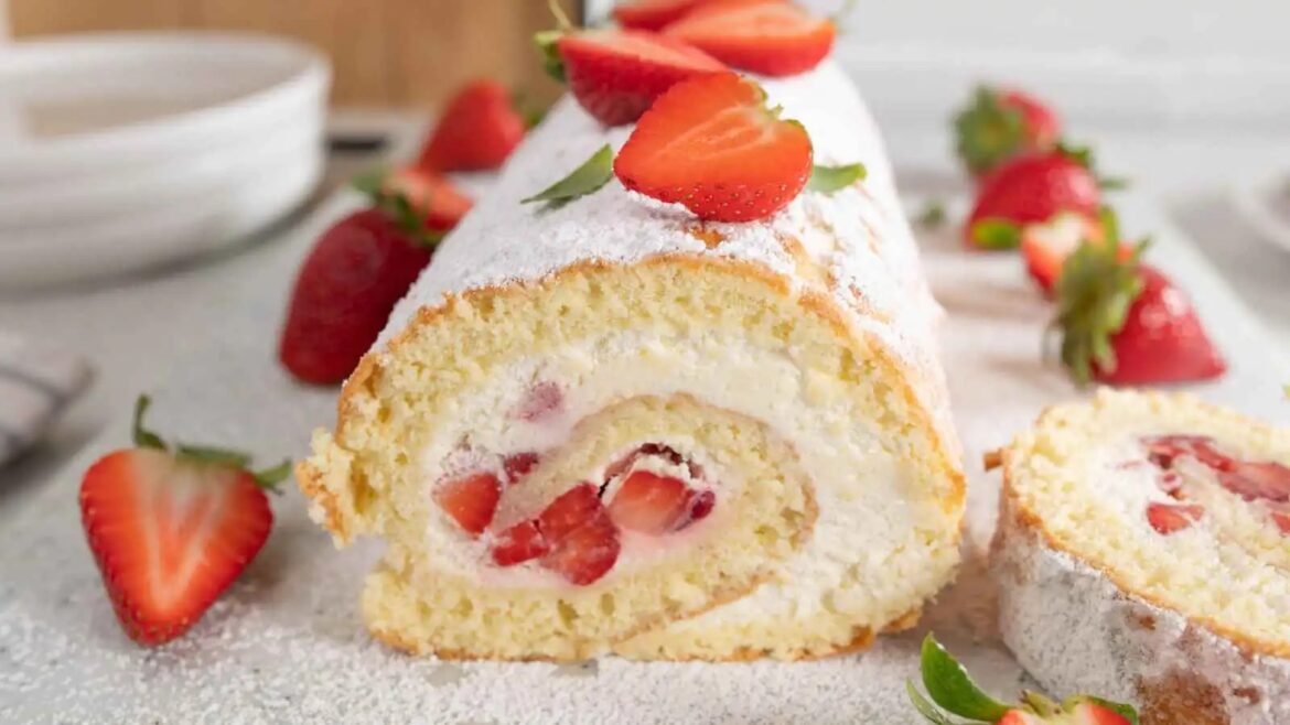 Strawberry-filled cream Swiss roll dusted with powdered sugar and topped with sliced strawberries on a white surface