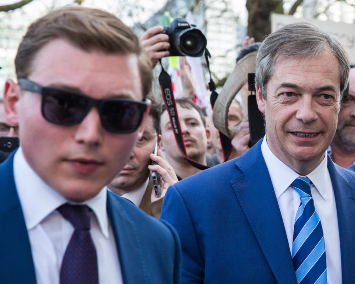 Two men in blue suits walk through a crowd of photographers at a public event.