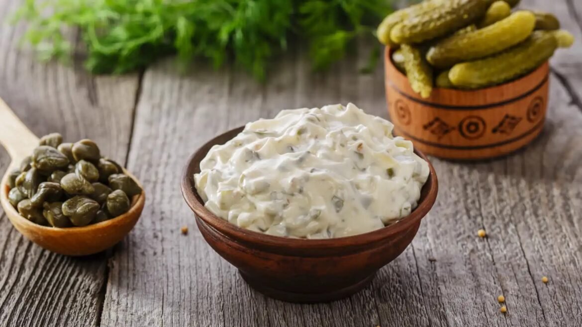 Creamy herb dip in a wooden bowl with chopped dill, surrounded by pickles on a rustic wooden table.