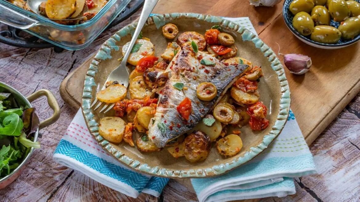 Mediterranean-style fish fillet with roasted potatoes, olives, and tomatoes on a rustic plate with herbs.