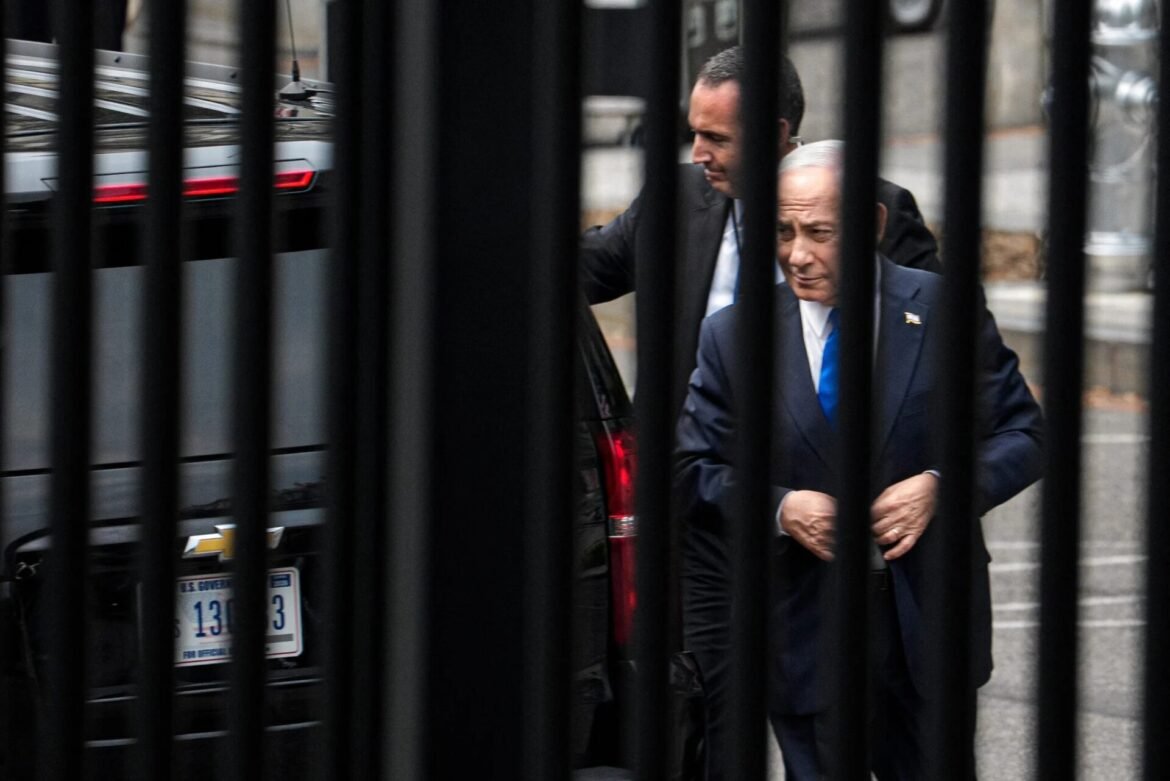 Two men in suits stand near a parked car behind vertical metal bars, one guiding the other through a gated area.