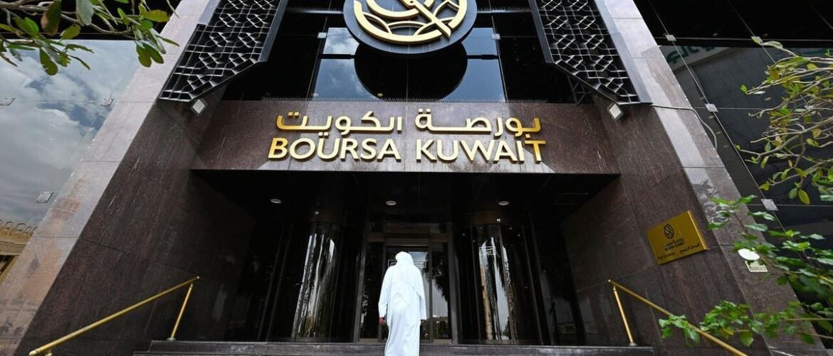 Entrance of Boursa Kuwait stock exchange building with gold sign, a person in a white thawb walking toward doors.