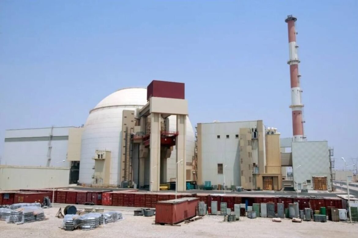 Nuclear power plant with a large white dome and a tall red-and-white smokestack, surrounded by equipment and containers on the ground.