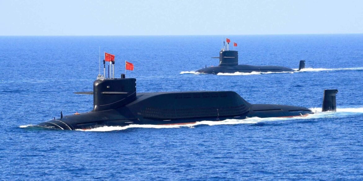 Three Chinese Navy submarines sailing on the surface in the blue ocean, red flags fluttering from their conning towers.