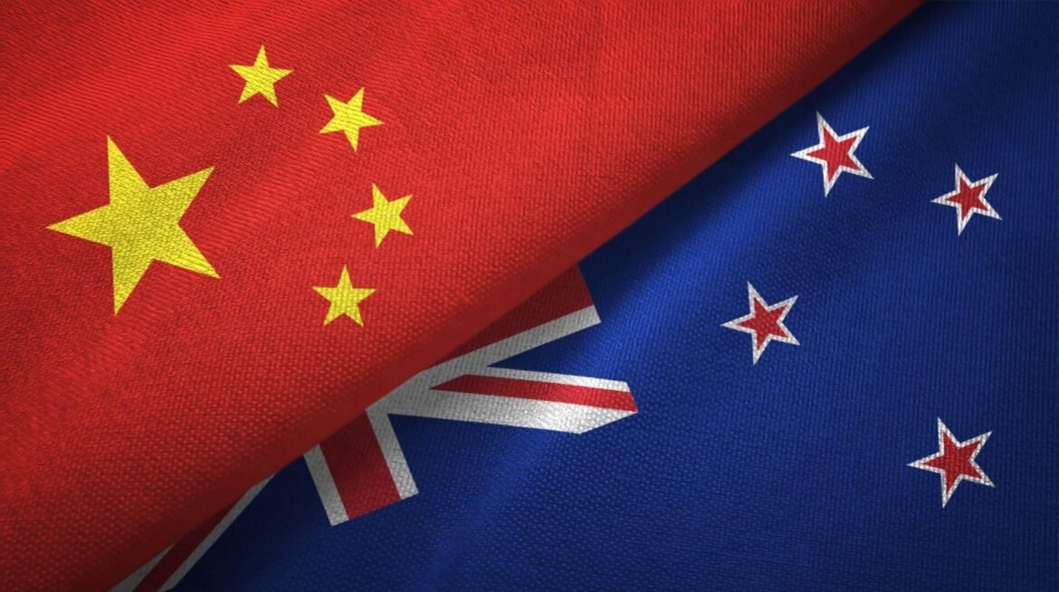 Overlapping national flags: China's red field with yellow stars partially covers New Zealand's blue flag with the Union Jack and red stars on fabric.