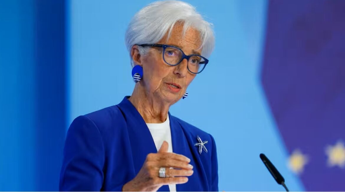 Senior woman in a blue blazer speaking at a podium, gesturing with her hand against a blue backdrop.