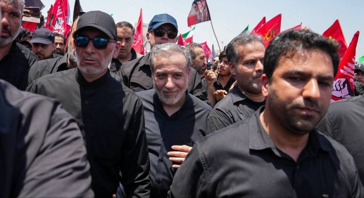 A crowd of men in black clothing marching at a protest, with red flags in the background.