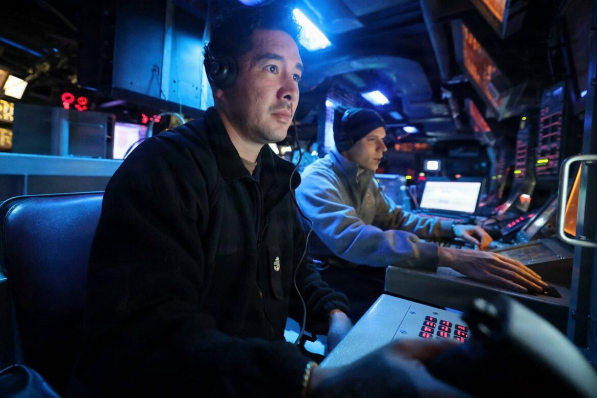 Two technicians in a dim, blue-lit control room wearing headsets and monitoring consoles.