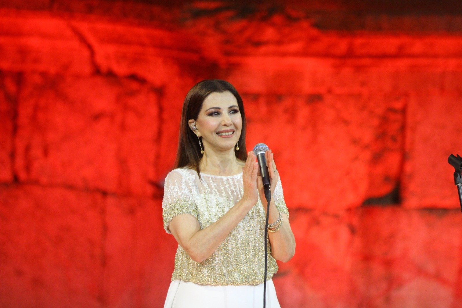 Woman in a Sparkling Beige Top Sings into a Microphone on a Red lit Stage with a Blurred Red Backdrop Behind Her  Aleumumnews