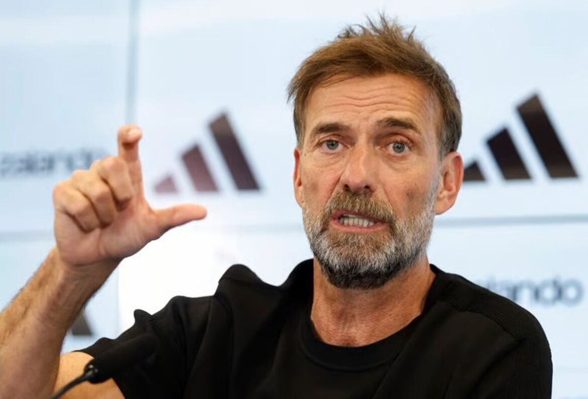 Man with gray beard in a black shirt speaks at a press conference, framing a point with his hands.