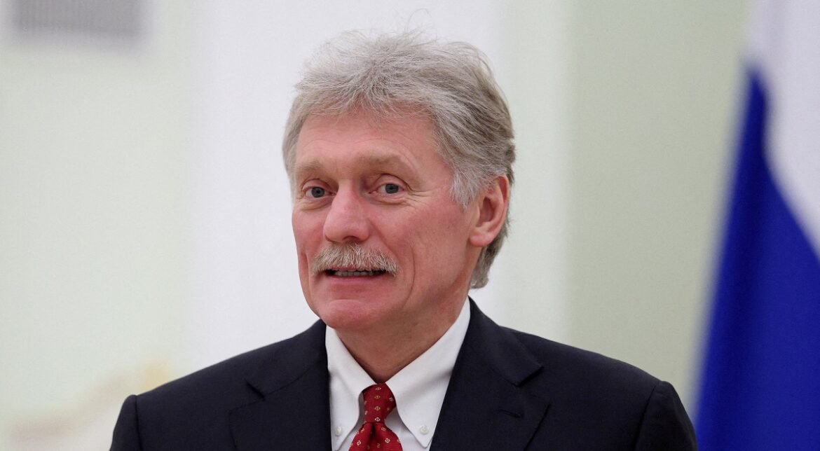 Portrait of a senior man in a dark suit and red tie, looking toward the camera in an indoor setting.