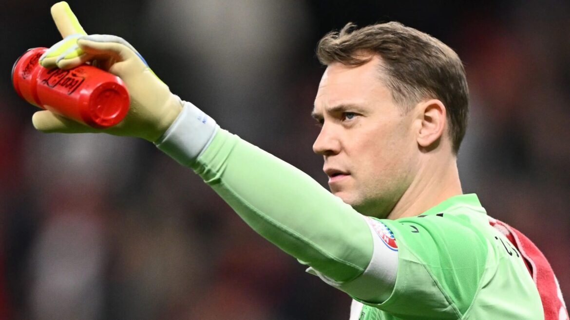 Soccer goalkeeper in a bright green kit raises a red water bottle while pointing with gloved hand to teammates.