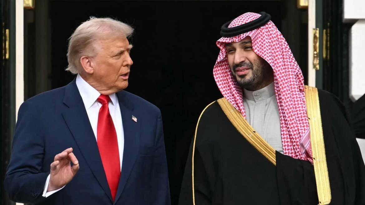 Two men in formal attire stand at a doorway, conversing; left man wears a navy suit with a red tie, right man wears traditional Saudi attire with a red-and-white checkered headscarf and black cloak.
