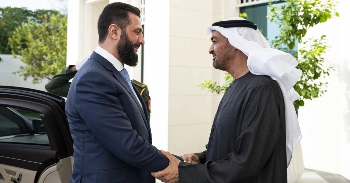 Two men shake hands outside a building: a suited businessman with a beard and a man in traditional Arab dress beside an open car door.