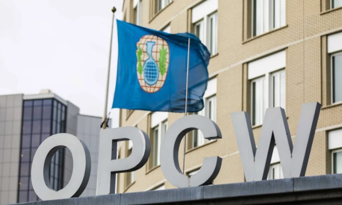 Blue flag with the OPCW emblem flies above large white OPCW letters on a city building façade.