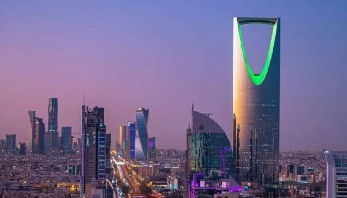 Riyadh skyline at dusk featuring the Kingdom Centre with a green arch at the top.