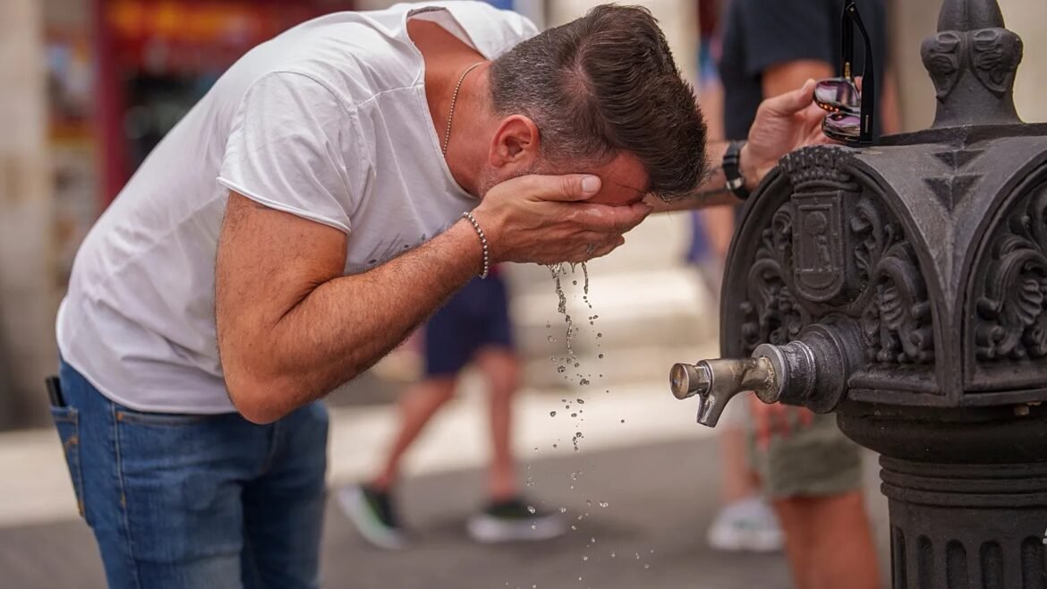 Man rinsing his face at a decorative street fountain in a city setting.