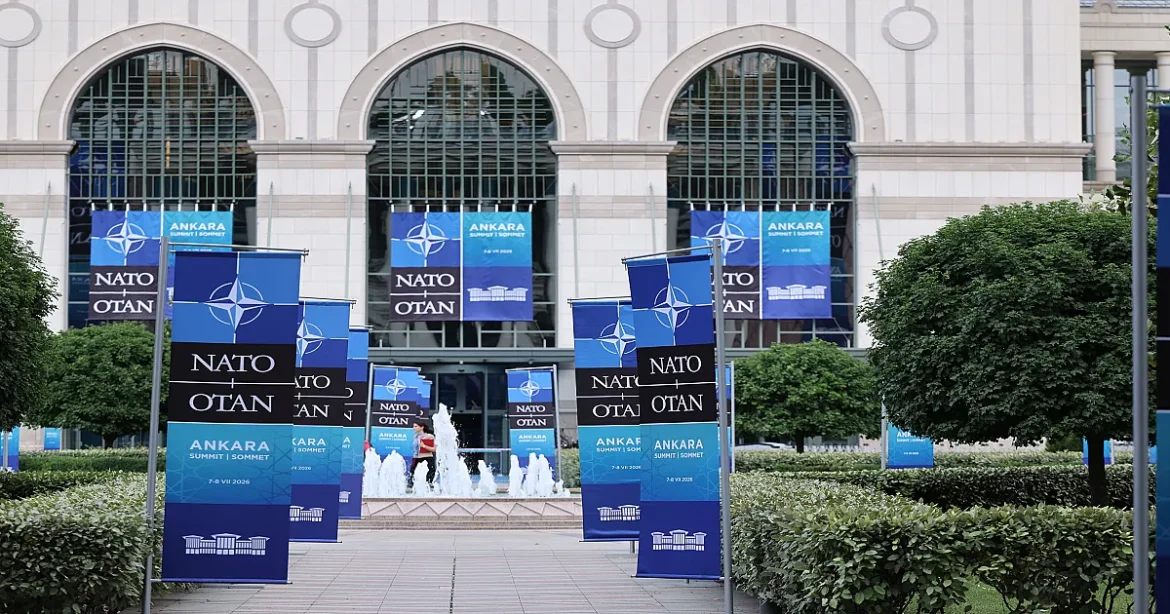 Blue NATO banners line a plaza in front of a grand government building with a fountain.