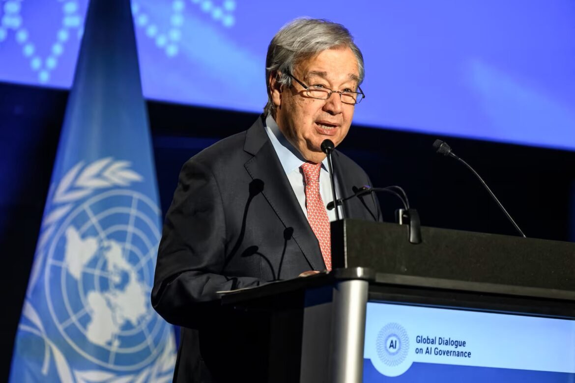 Speaker in a suit and red tie delivering remarks at a podium, UN flag beside him, screen reading 'Global Dialogue on AI Governance' in the background.